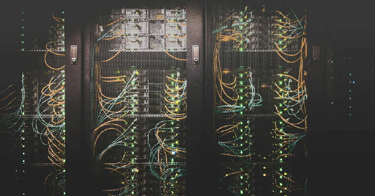 Server racks behind mesh doors with orange and teal network cables and green status lights