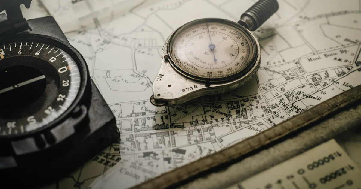 A black compass and a silver map-measuring instrument with a dial, resting on an old black-and-white street map