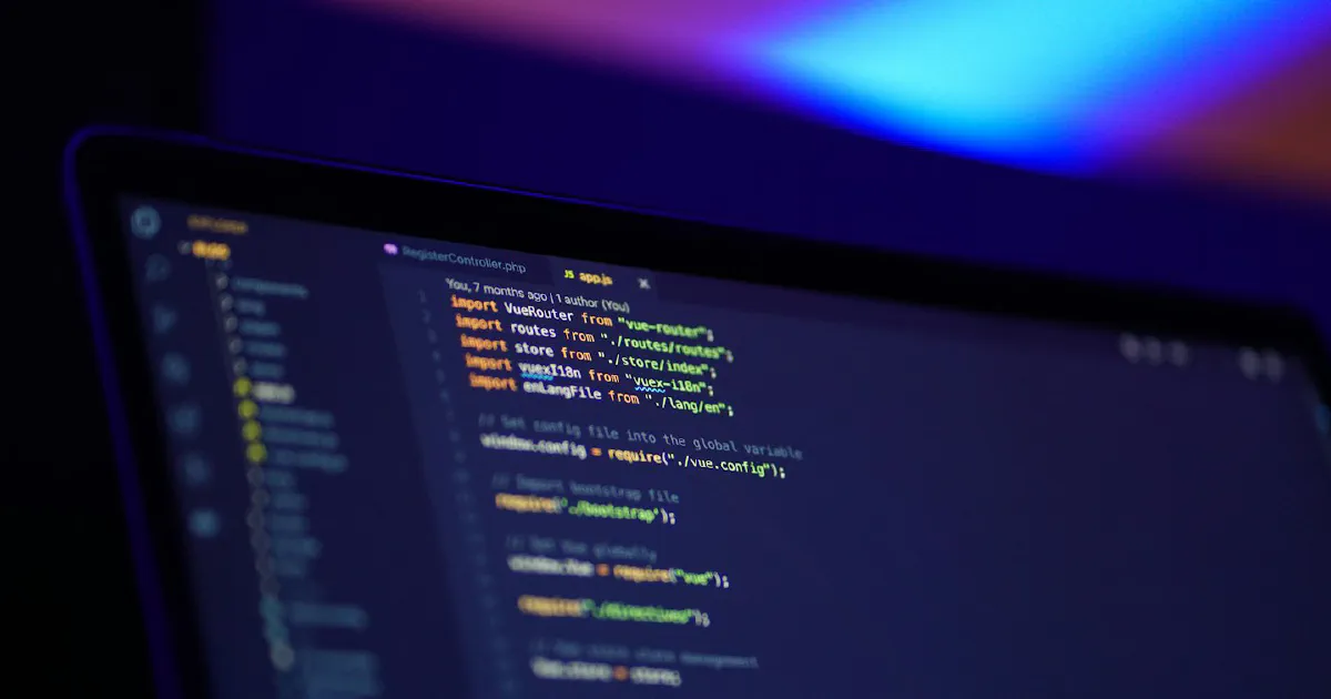 Blurred laptop screen in a dark room showing JavaScript code in a code editor