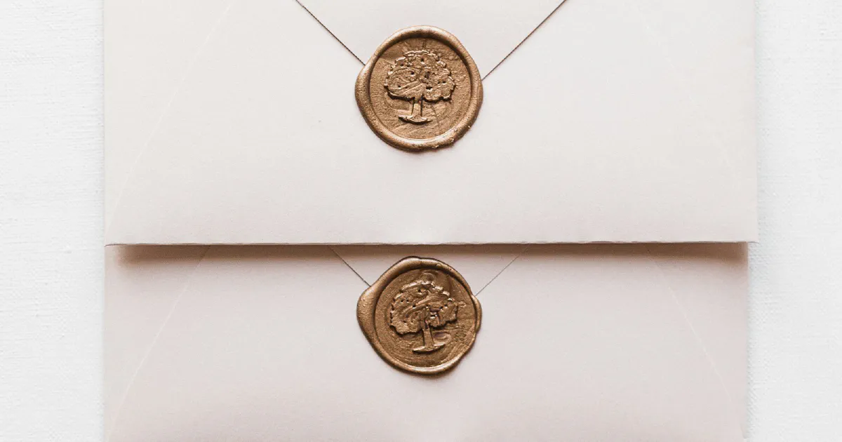 Three cream envelopes, each closed with a bronze wax seal stamped with a tree design, on a white surface